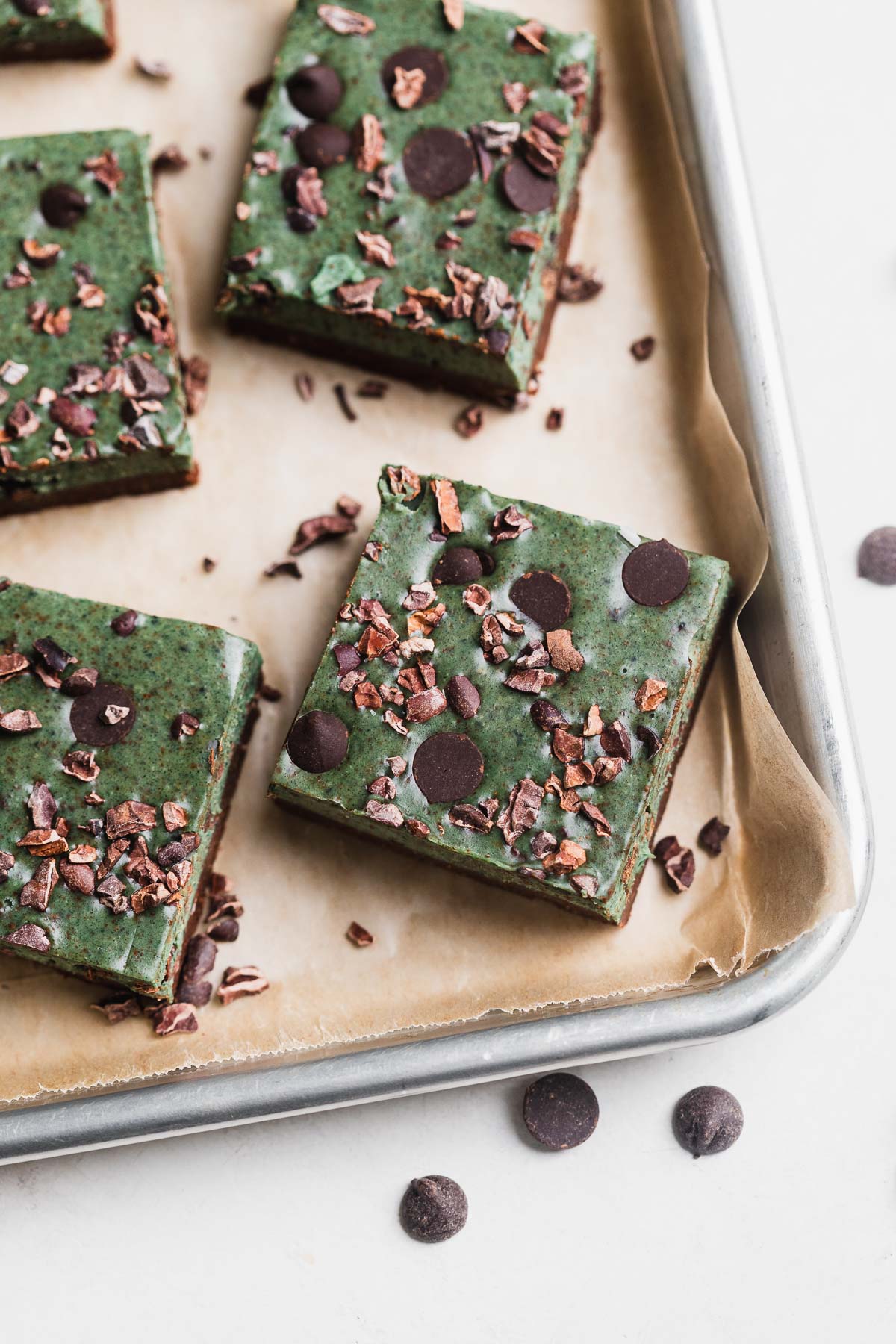 Green mint cookie bars on a baking sheet with chocolate chips. 