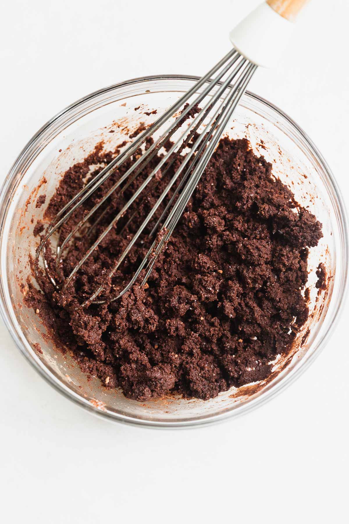 Gluten free cookie crust in a glass mixing bowl with a whisk in it.