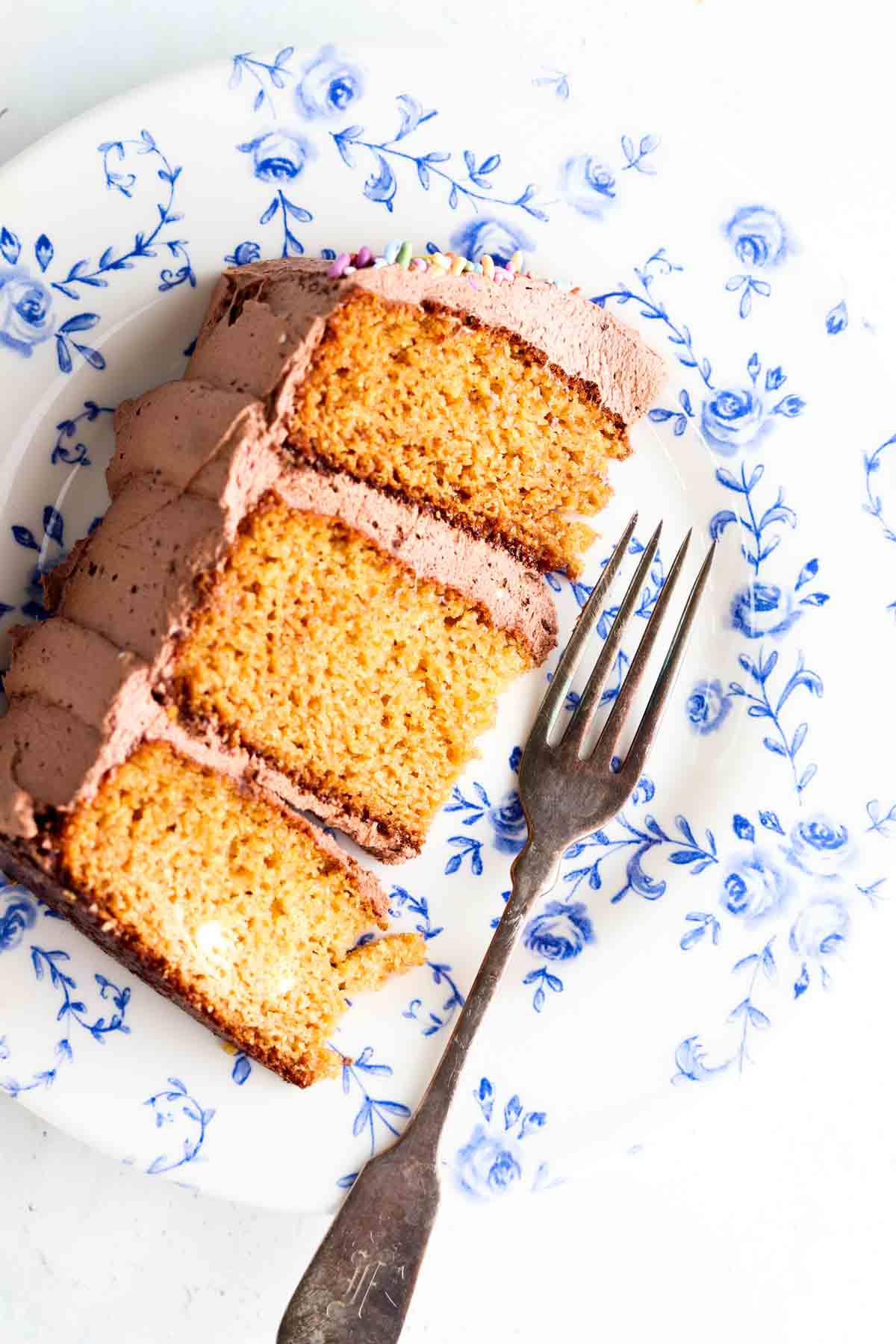 Slice of a 3 layered vanilla cake with chocolate frosting.