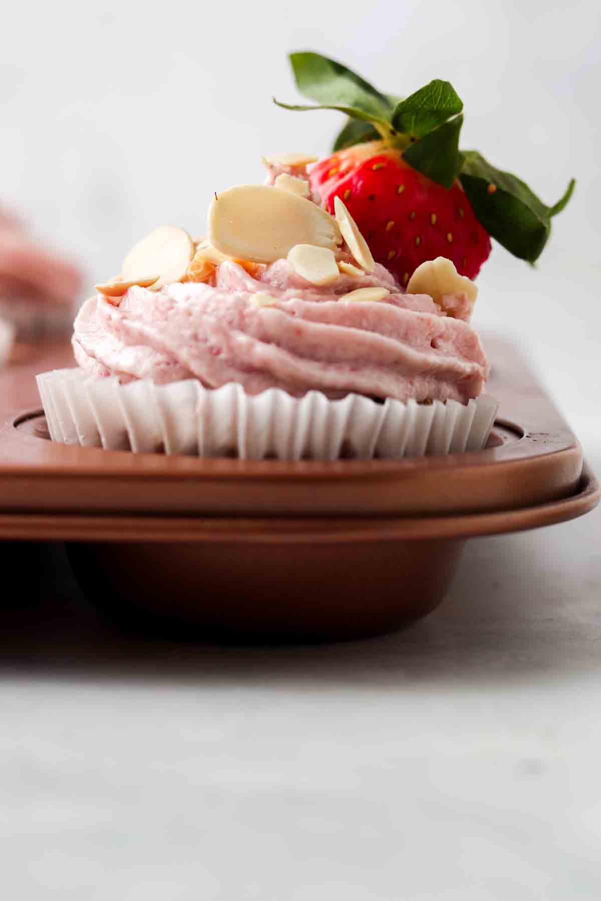 Strawberry cupcakes in cupcake pan with almond slivers and fresh strawberry garnish. 