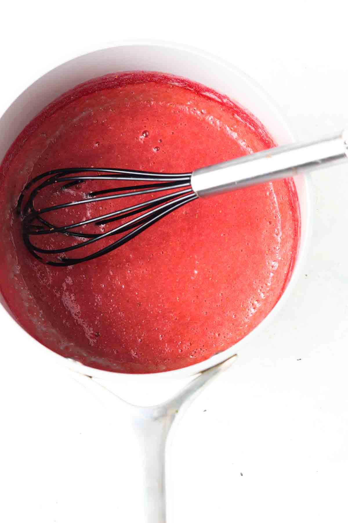 Strawberry sauce in a sauce pan with a whisk.