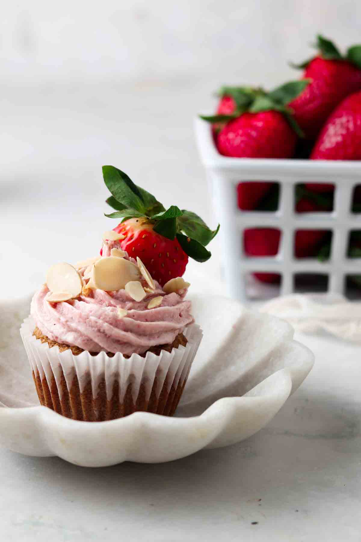 Strawberry cupcake with a strawberry on top on a small white plate. 