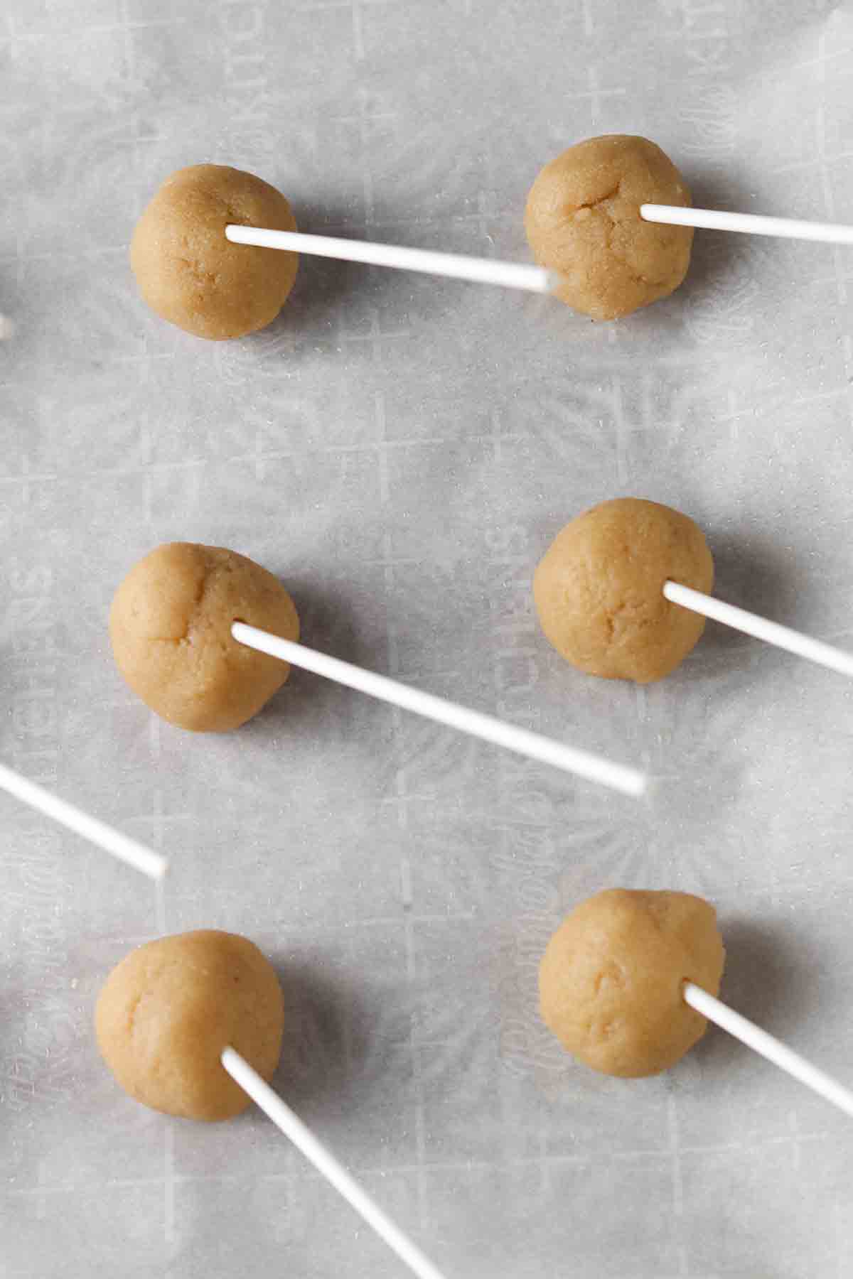Cake pop sticks stuck in the raw cake pops on a baking sheet. 
