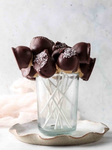 Cake pops on a stick in a blue cup with white sprinkles on top.