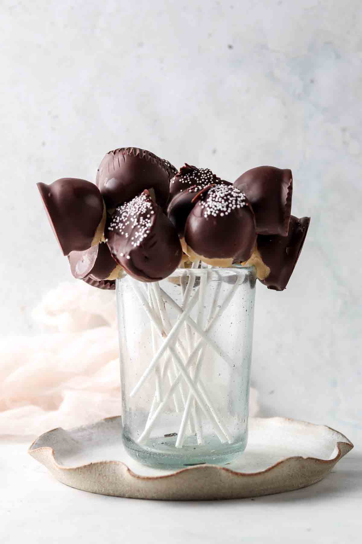 Cake pops on a stick in a blue cup with white sprinkles on top.