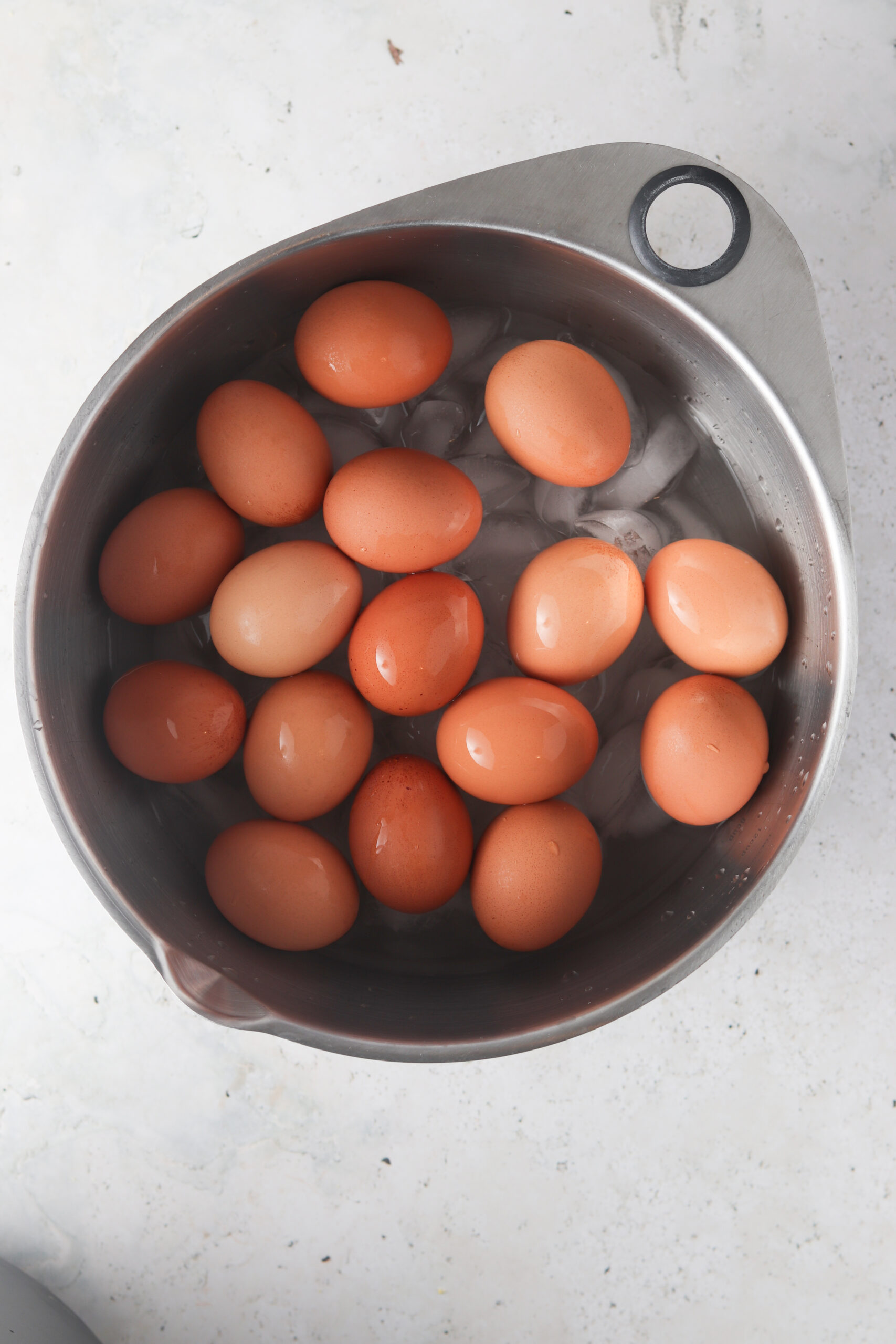 Hard boiled eggs in an ice bath in a metal bowl.