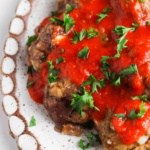 Gluten free meatballs on a white plate covered in red sauce and parsley.