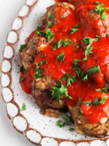 Gluten free meatballs on a white plate covered in red sauce and parsley.