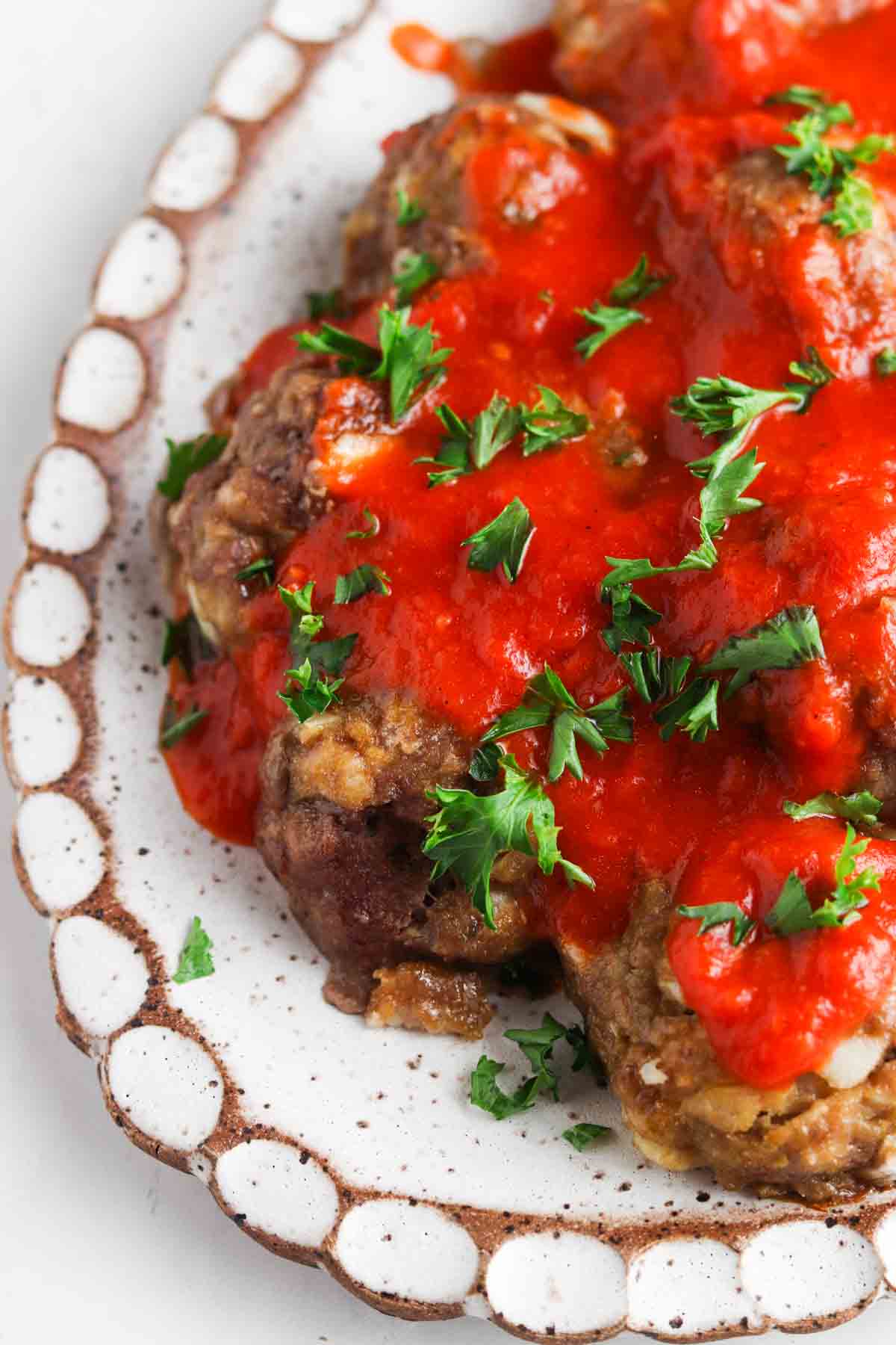 Gluten free meatballs on a white plate covered in red sauce and parsley.