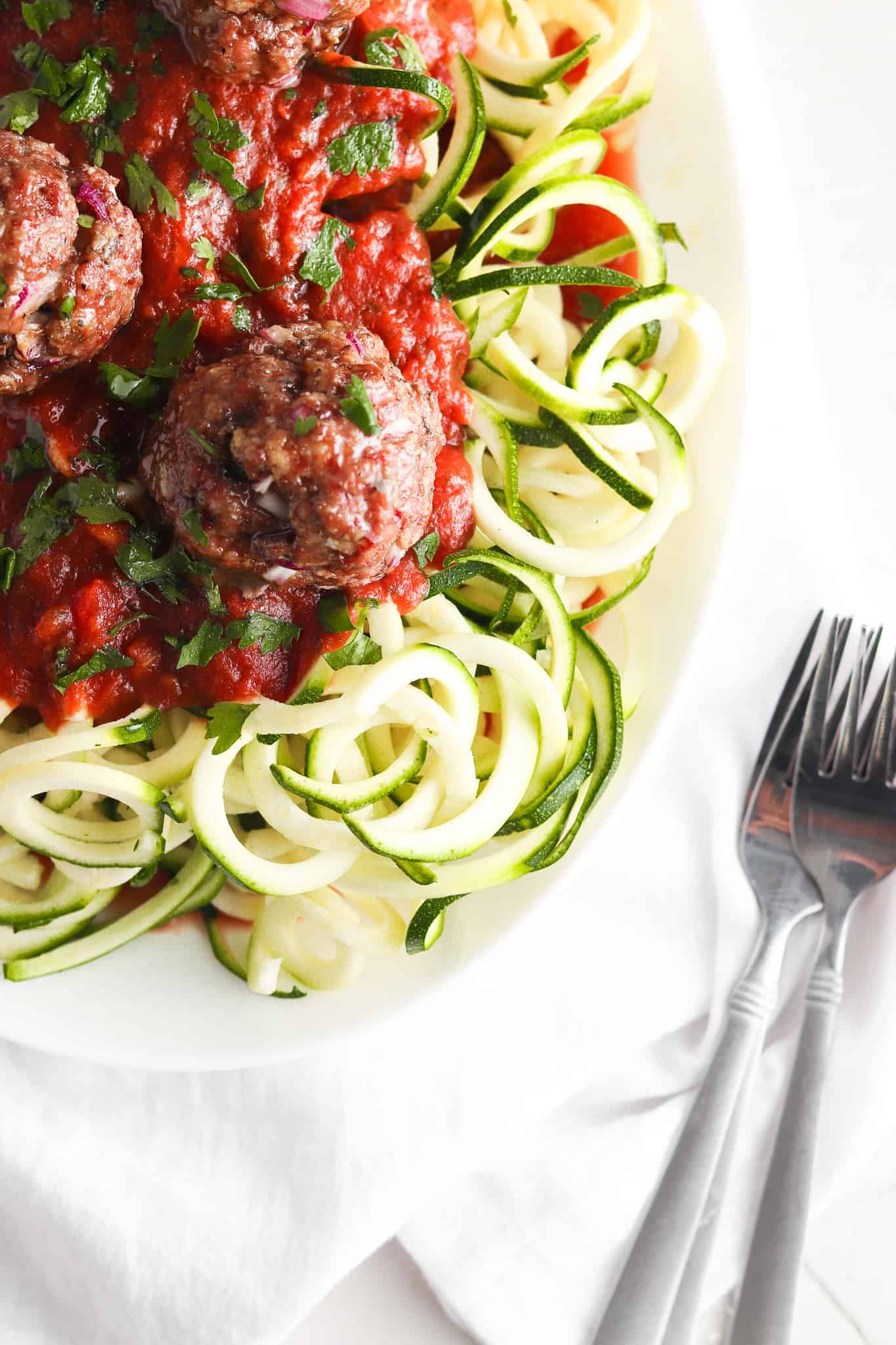 Spaghetti and gluten free meatballs on a white plate with forks. 