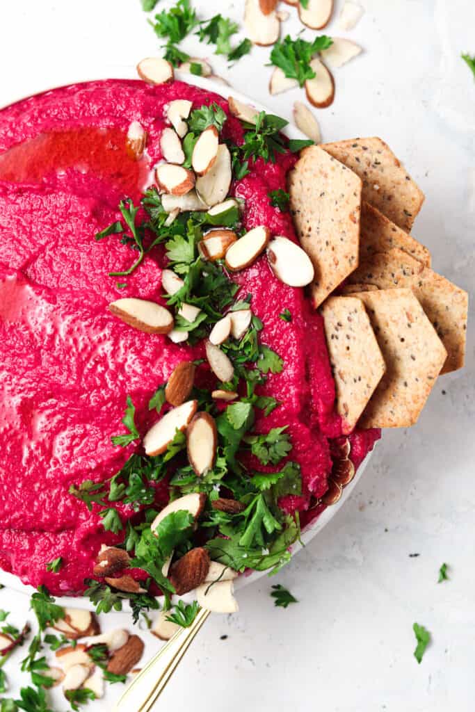 Close up of paleo beet hummus with crackers, almond slivers, and parsley.