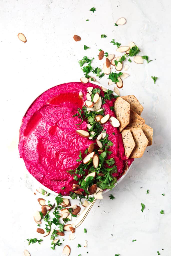 Paleo beet hummus on a countertop with almonds and parsley.