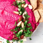 Beetroot dip on a plate with crackers and fresh parsley on top.