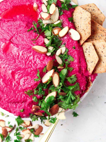 Beetroot dip on a plate with crackers and fresh parsley on top.