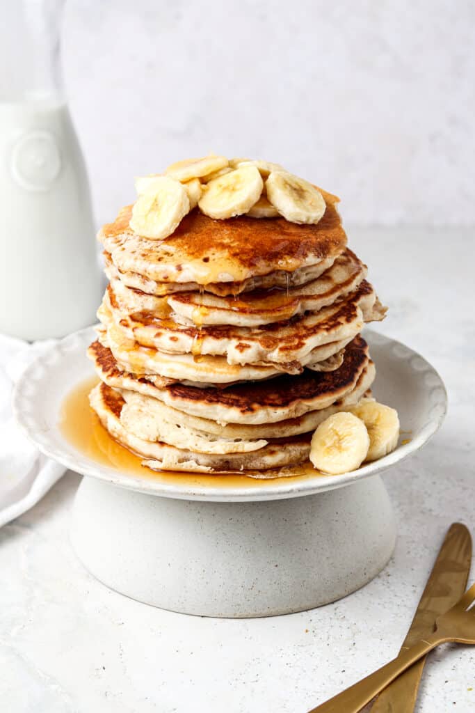 3 ingredient protein pancakes stacked on a plate with bananas and maple syrup