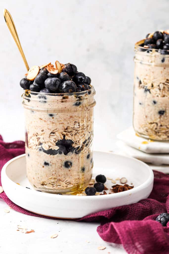 blueberry banana overnight oats in a mason jar on a white plate with a gold spoon