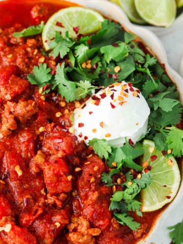 close up photo of chili in a bowl with limes