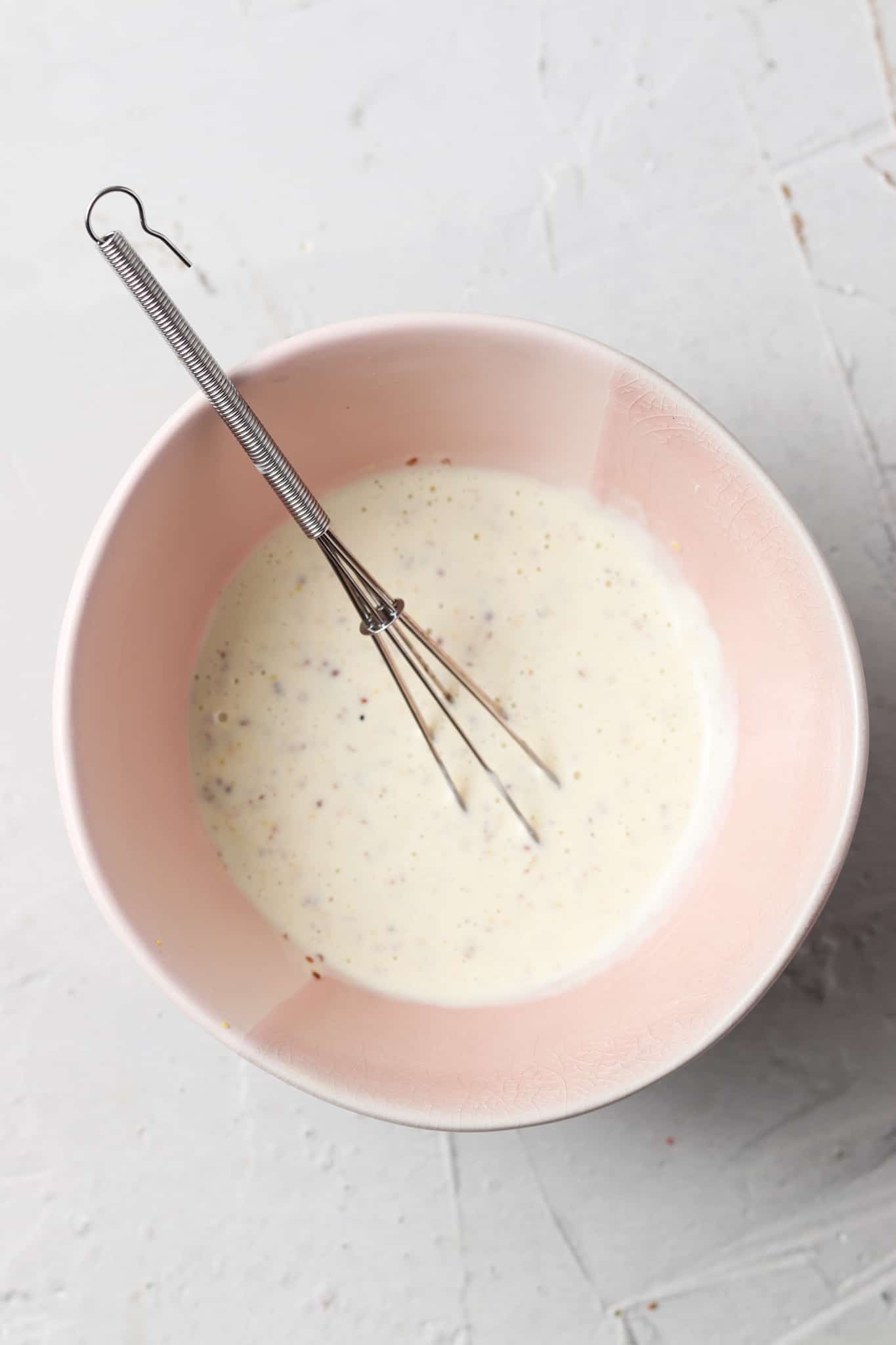 Avocado mayo, dijon mustard, garlic, and lemon juice in a pink bowl with a whisk.