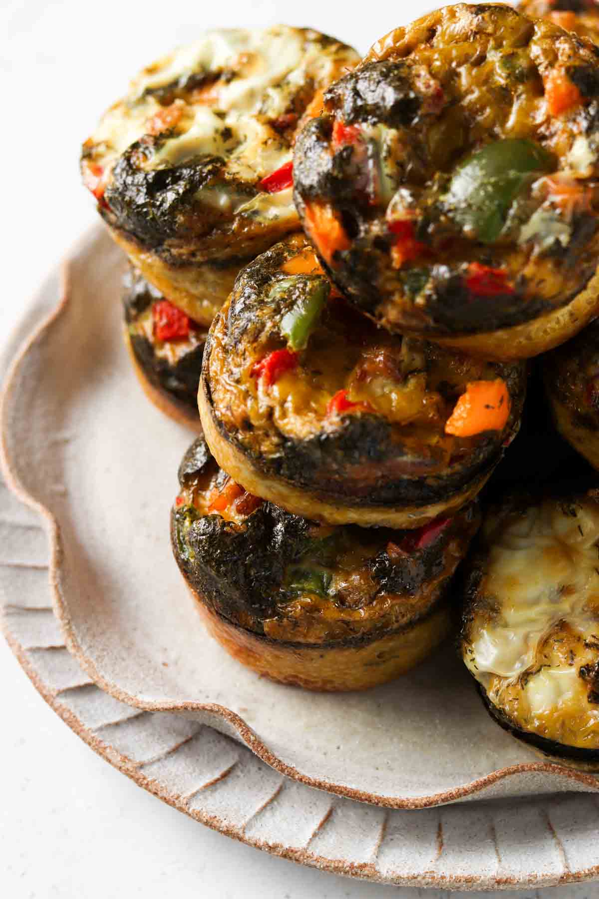 Egg muffins with dill and peppers on top on a ruffled plate on the counter.