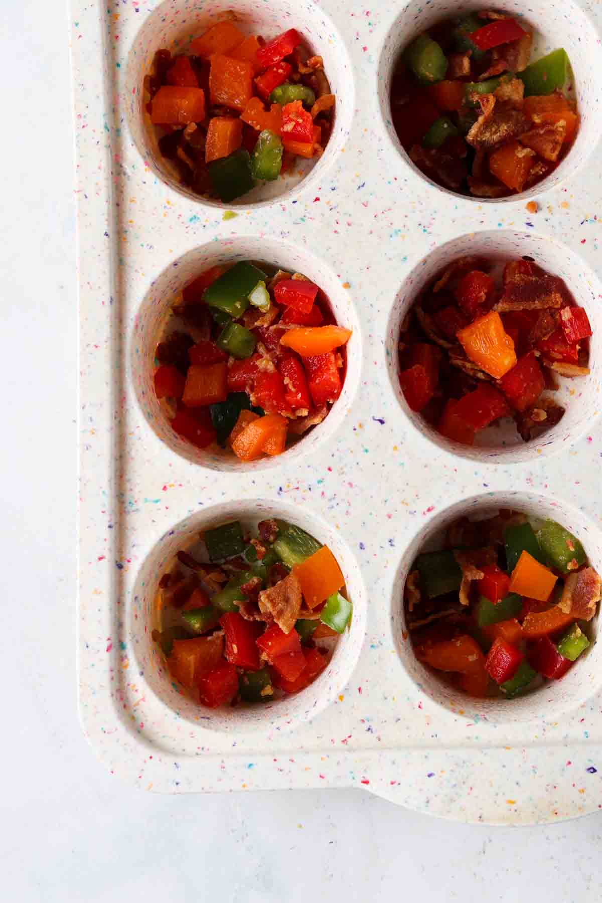 Chopped peppers and chopped bacon in small silicone muffins cups. 