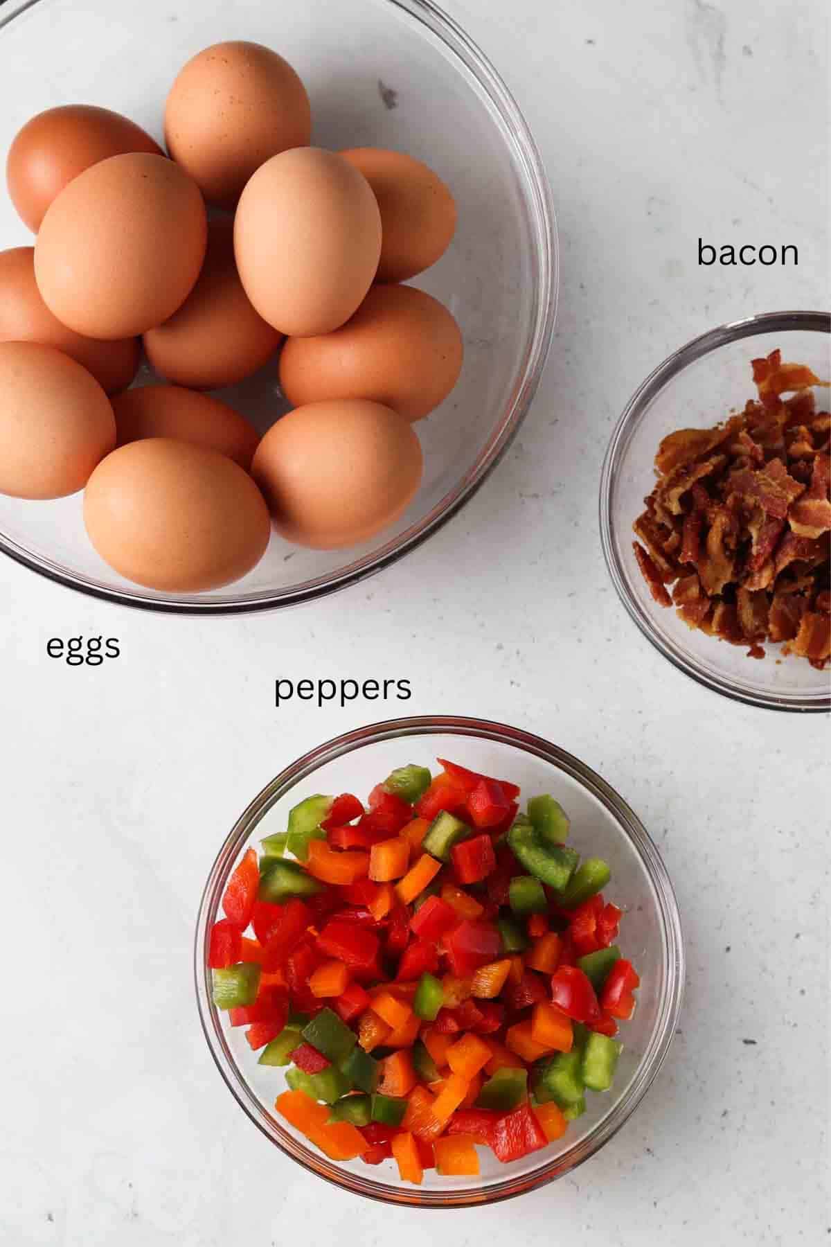 Eggs, chopped bacon and chopped peppers in small glass bowls. 
