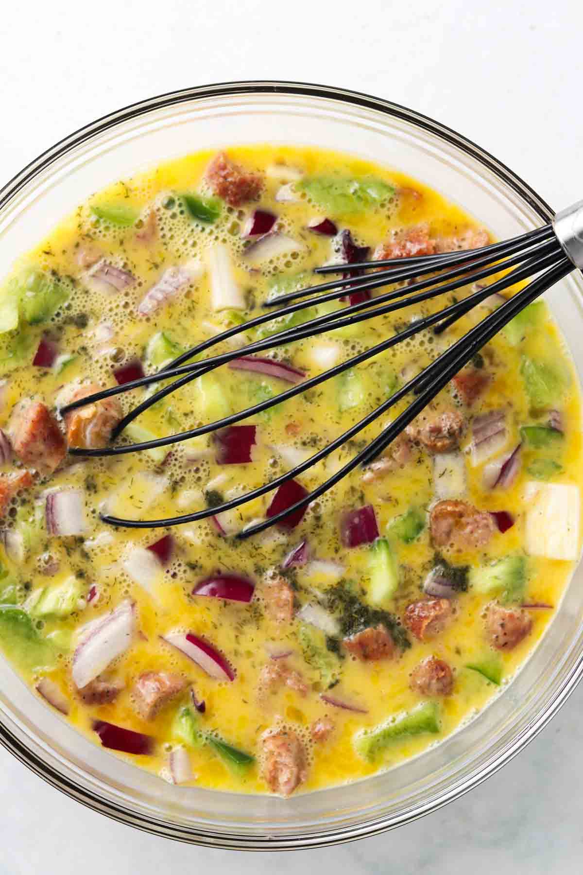 Eggs, peppers, onions and sausage in a glass bowl.