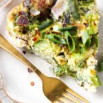 Close up picture of a pie shaped frittata on a plate with a gold fork on top.