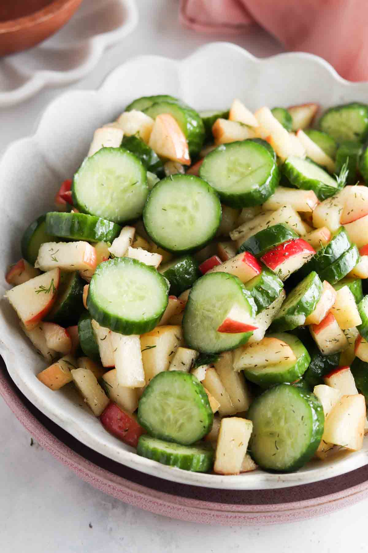 Mixed apples and cucumbers in a scalloped bowl with a dill dressing over top.