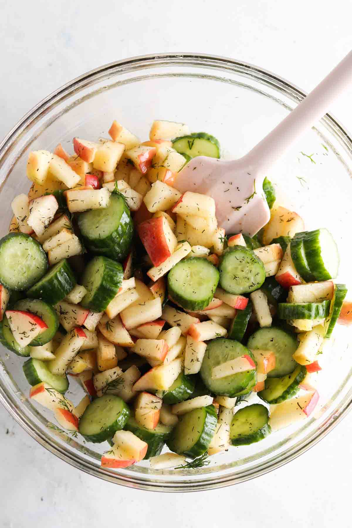 Cucumbers, apples, and dressing mixed together in a bowl.