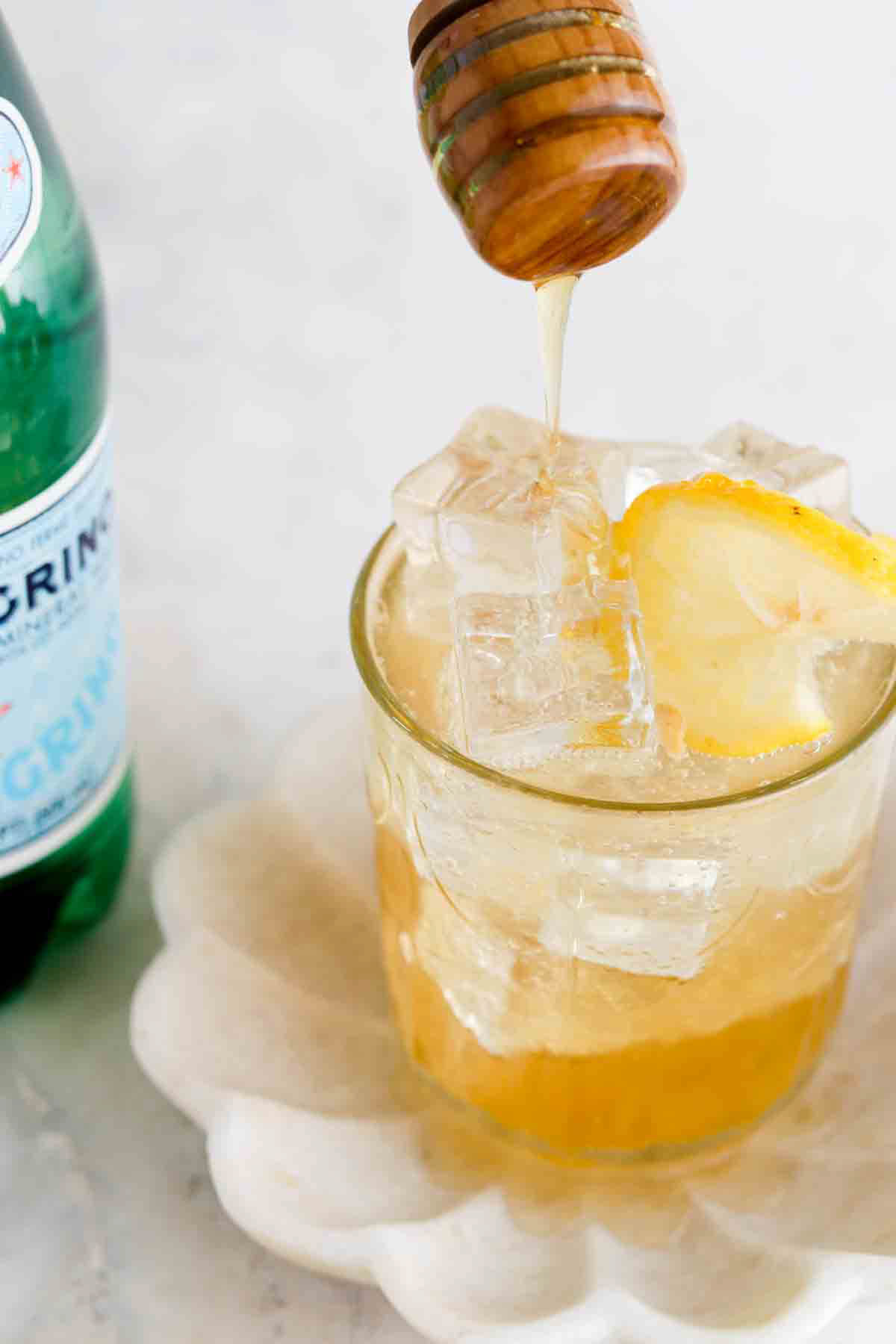 Honey dripping into a glass of a ginger mocktail with a green bottle of sparkling water next to it. 