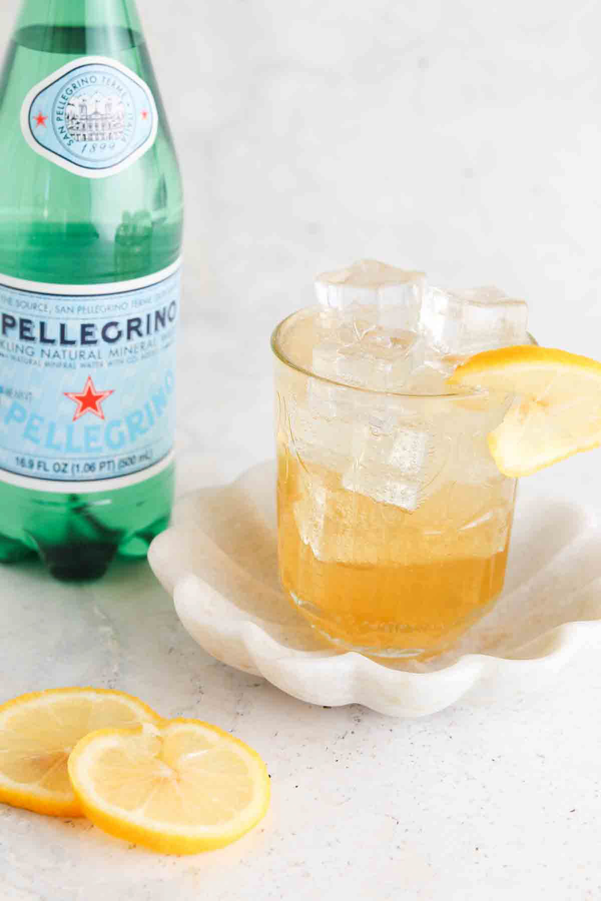 Ginger mocktail in a glass with a lemon on top and a bottle of pellegrano sitting next to it.