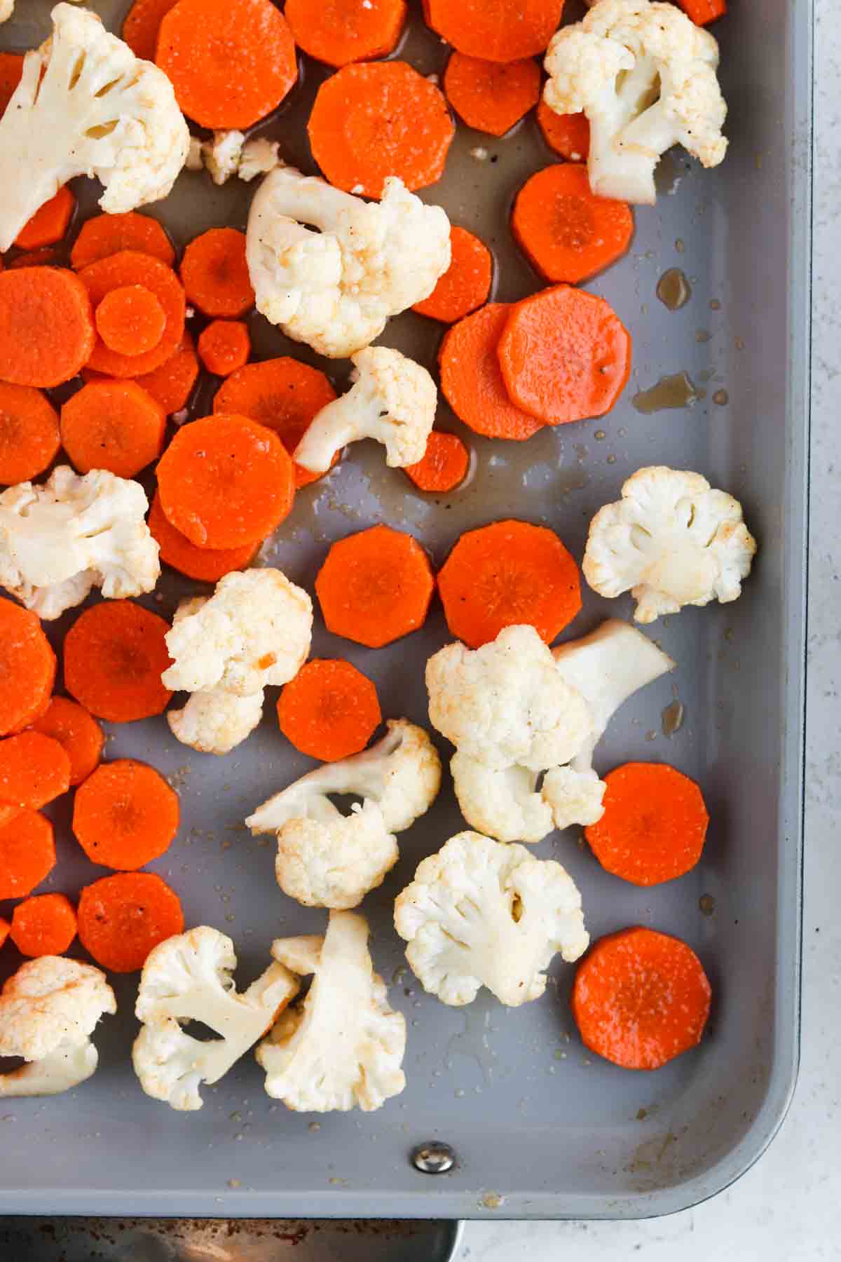 Cauliflower, and coined carrots laid out on a sheet pan.
