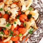 Roasted cauliflower and carrots on a brown plate with fresh parsley on top.