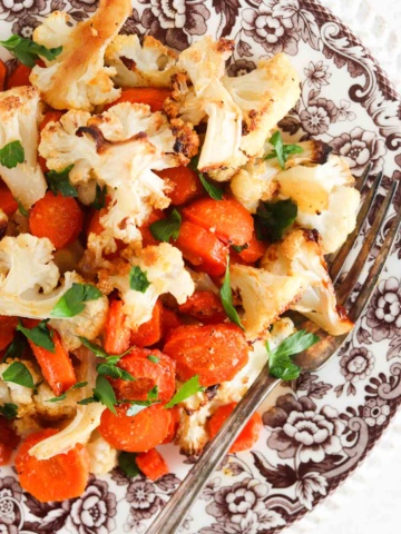 Roasted cauliflower and carrots on a brown plate with fresh parsley on top.