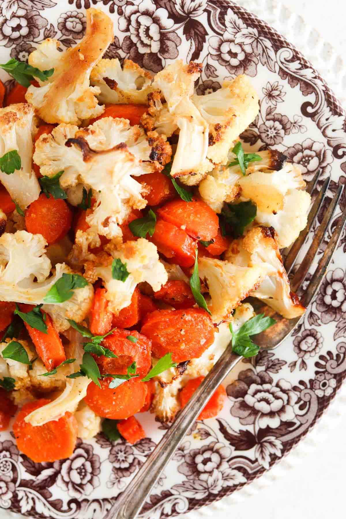 Roasted cauliflower and carrots on a brown plate with fresh parsley on top.
