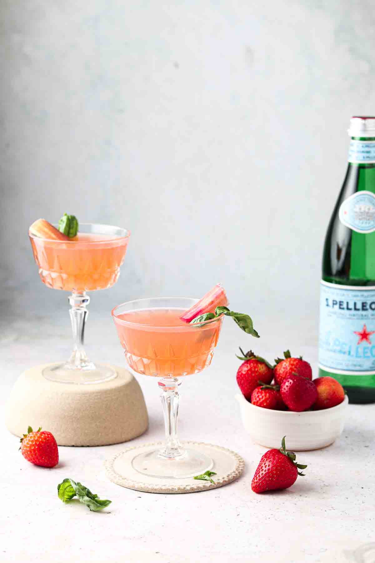 Rhubarb simple syrup mixed with club soda in glass cups garnished with fresh rhubarb and green herb.