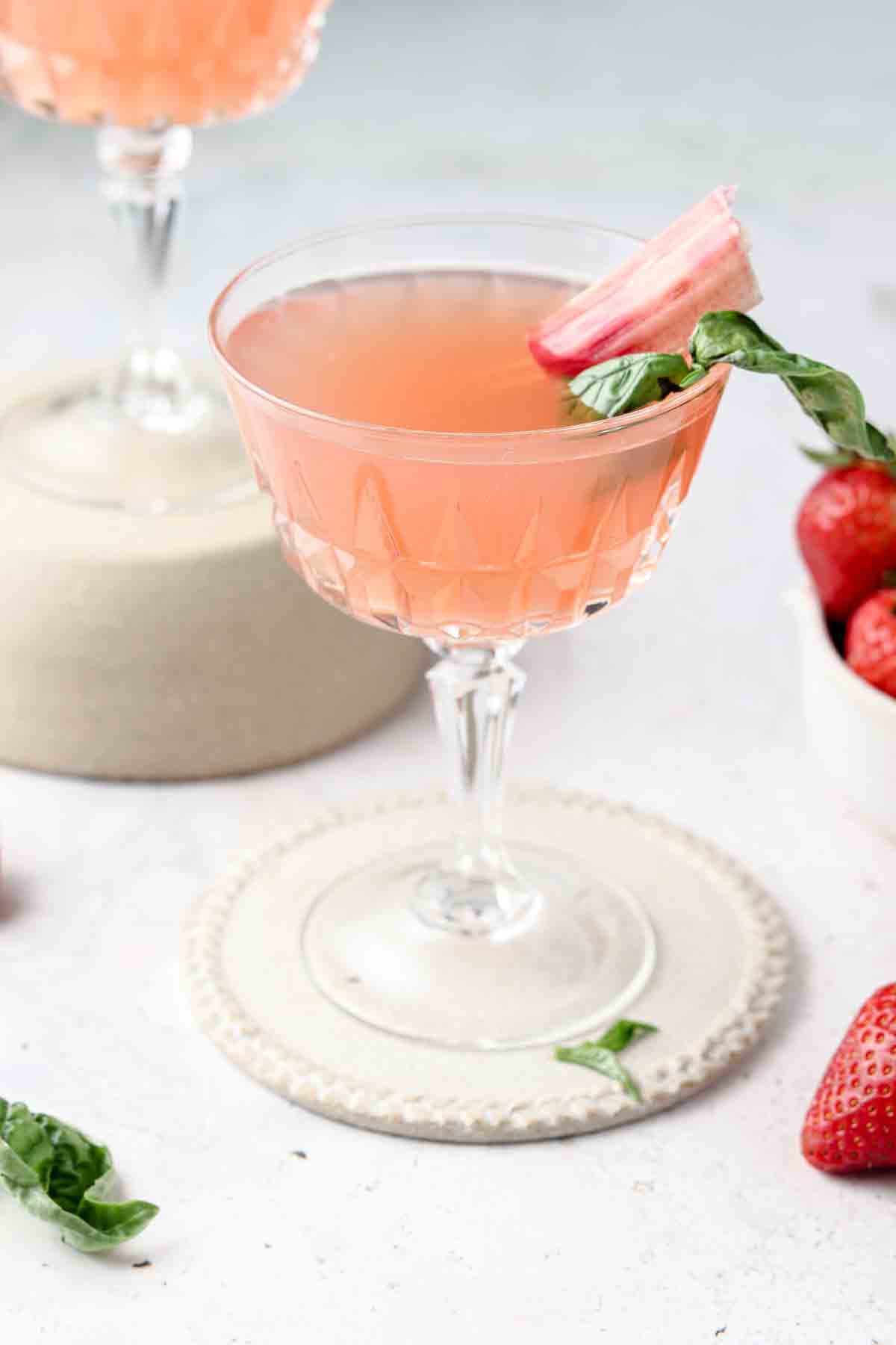 Rhubarb simple syrup in a glass with club soda, fresh rhubarb, and green basil.