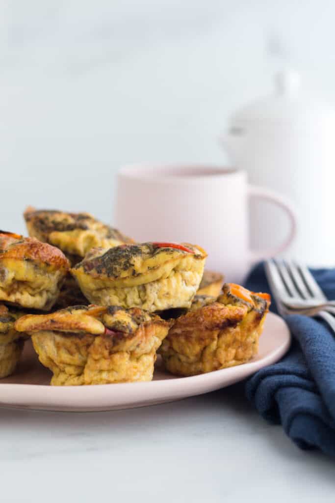 egg muffins on a pale pink plate with a navy blue napkin next to it and a coffee cup as well as a white pitcher