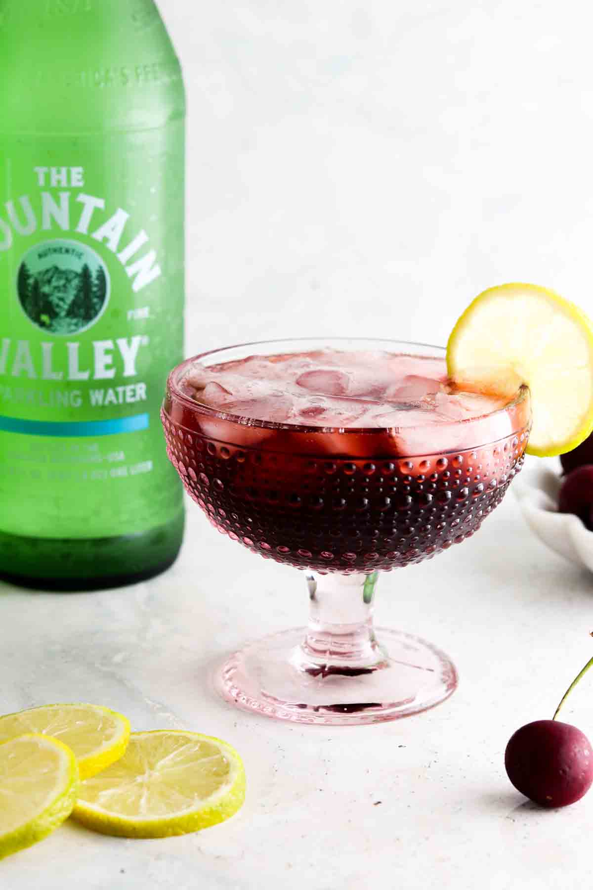 Cherry mocktail in a fun pink glass with a lime on top.