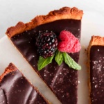 Gluten free tart with a silky chocolate filling on a plate with fresh berries and mint on top.