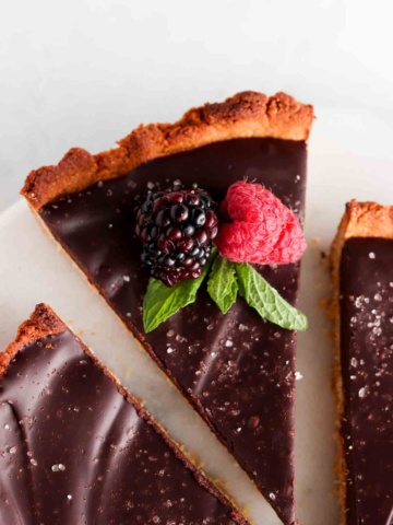 Gluten free tart with a silky chocolate filling on a plate with fresh berries and mint on top.