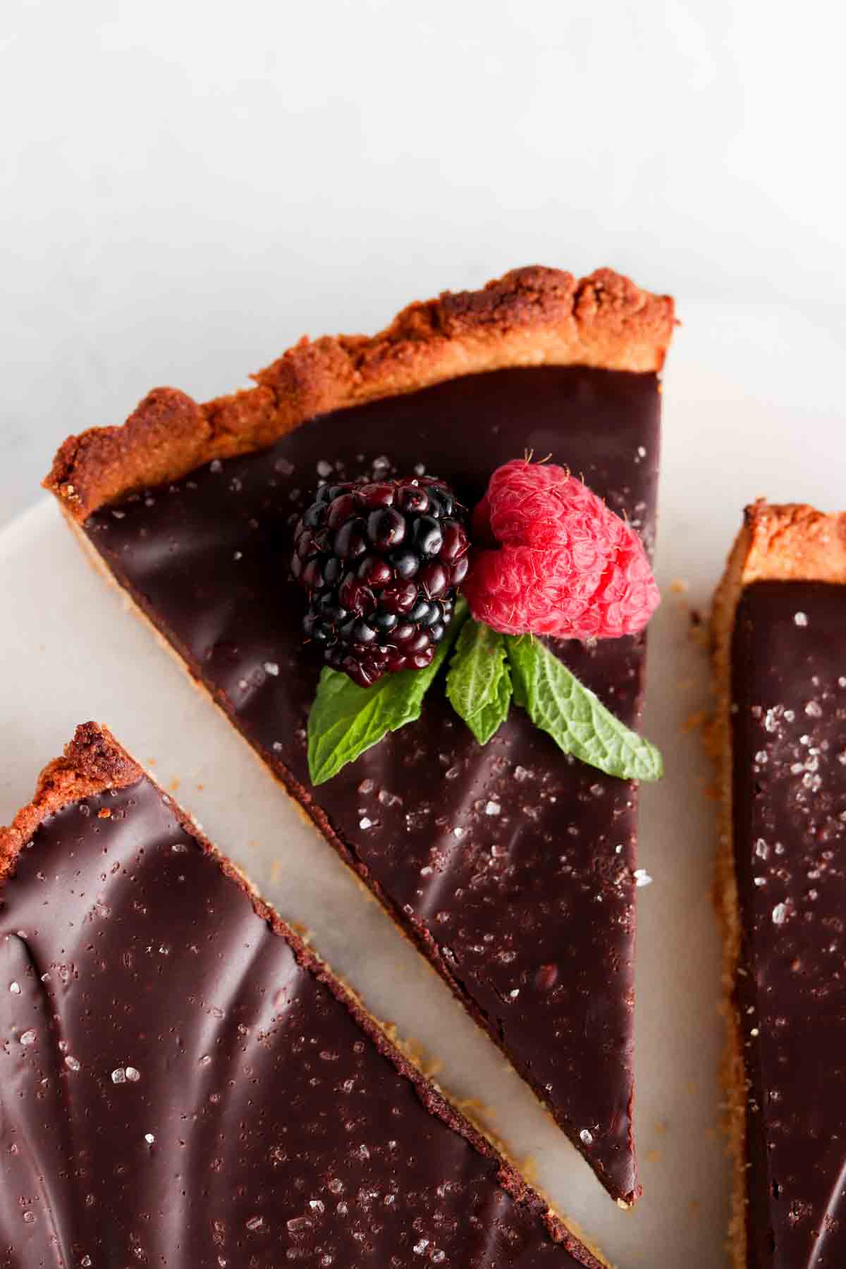 Gluten free tart with a silky chocolate filling on a plate with fresh berries and mint on top.