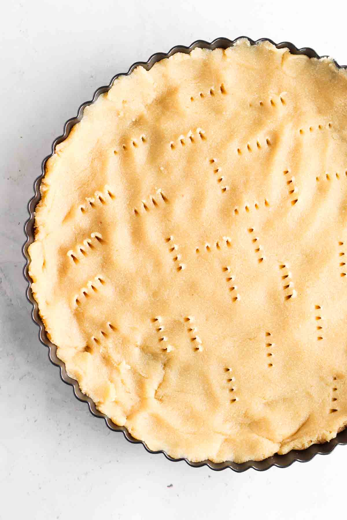 Gluten free tart crust in a tart pan with the crust having poked holes in it.