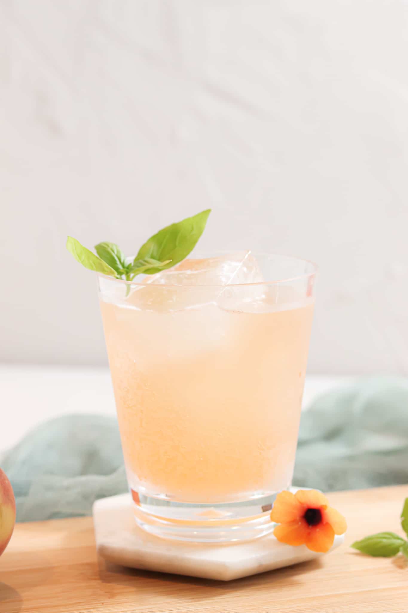 Peach basil mocktail in a glass cup with fresh green herb garnish. 