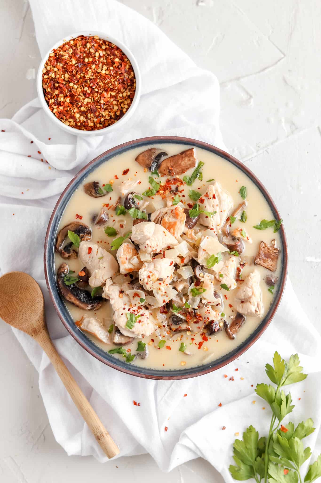 Thai Creamy Chicken Soup in a bowl garnished with red pepper flakes and fresh green herbs.