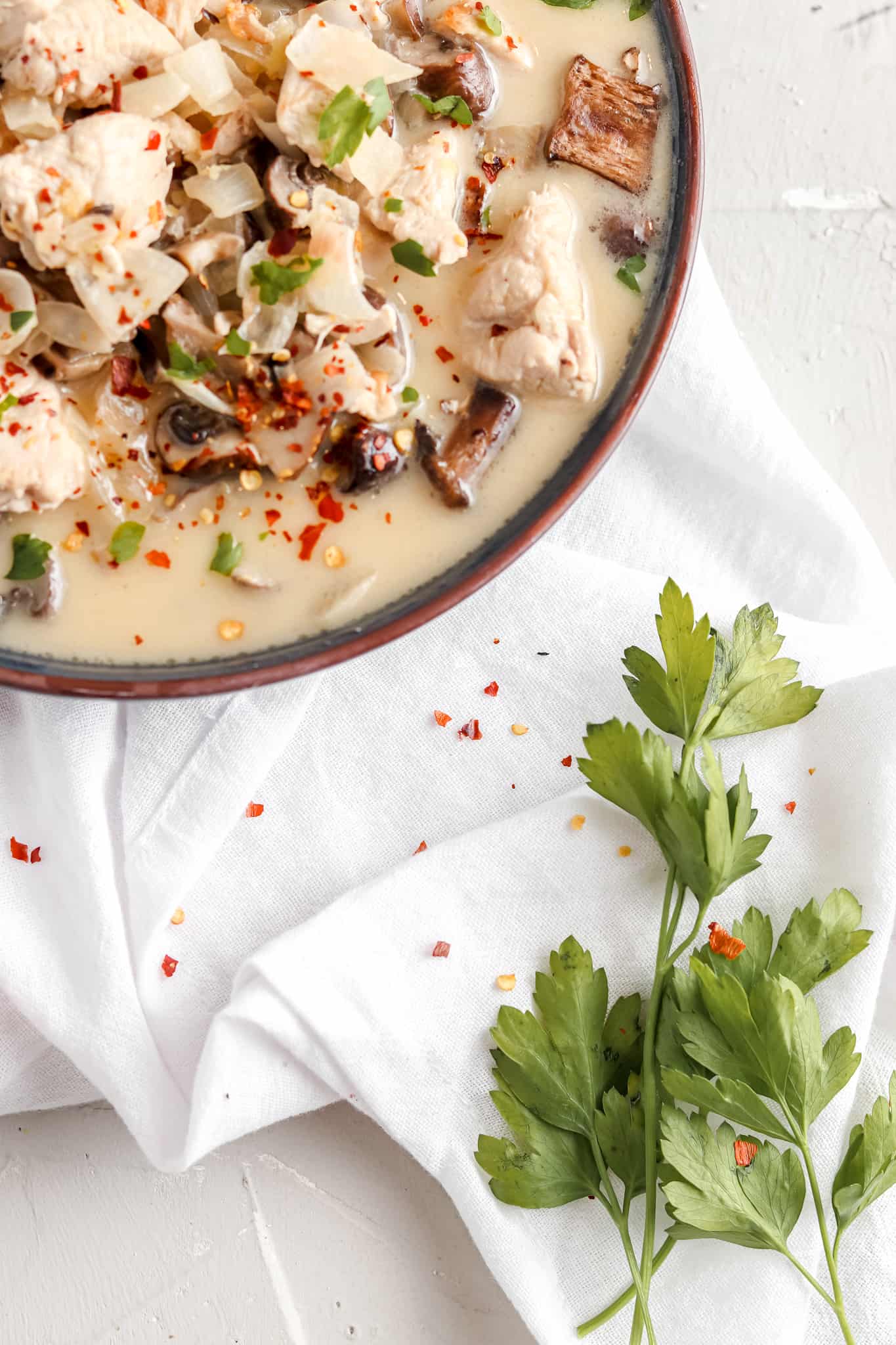 Creamy thai chicken soup in a dish and garnished with red pepper flakes and fresh green herbs.