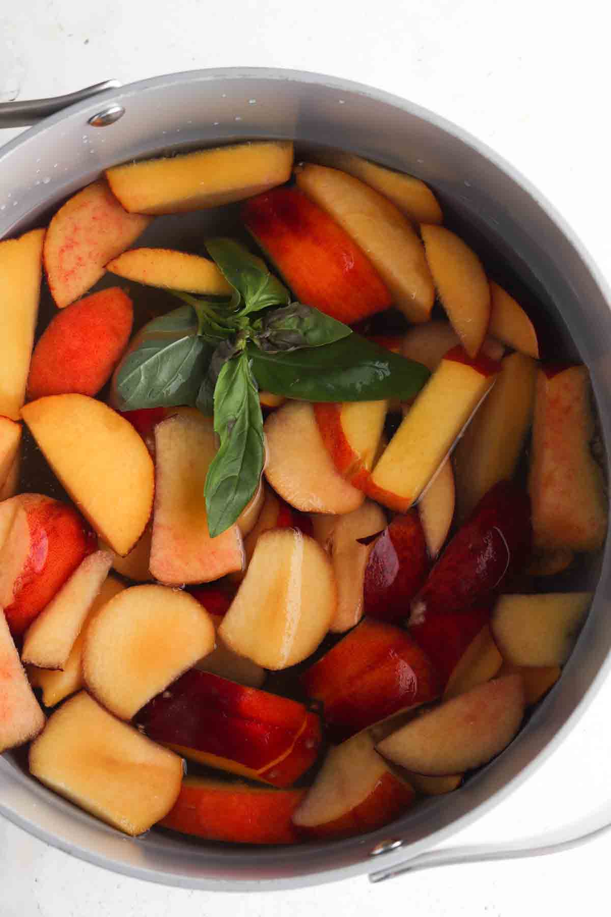 Sliced peaches, fresh basil, water, and honey in a bit pot.
