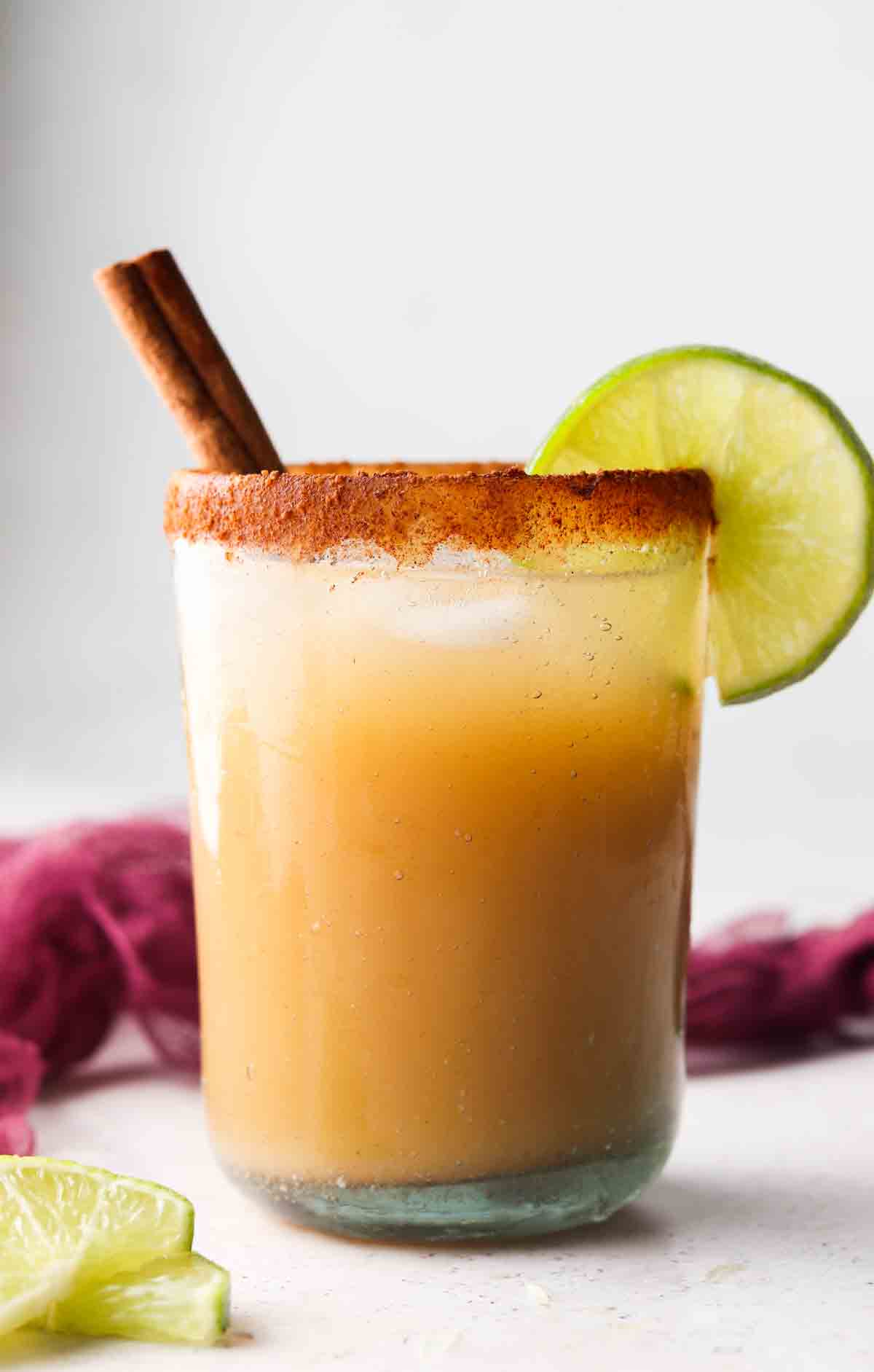 Apple cider margarita mocktail in a glass with a cinnamon stick hanging out of the side with a lime wedge. 