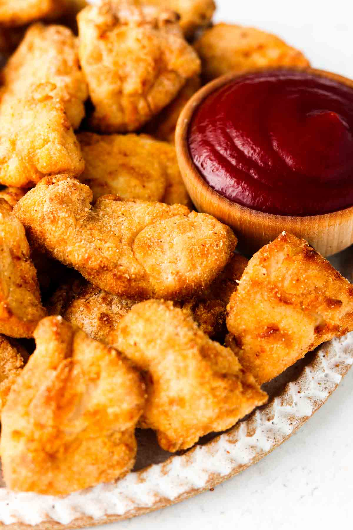 Crispy chicken nuggets on a plate with a small wooden bowl of ketchup.
