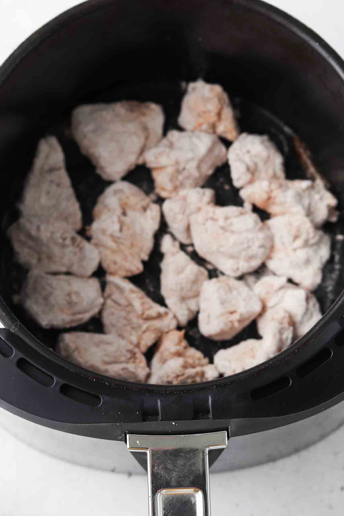 Raw chicken nuggets in an air fryer basket.